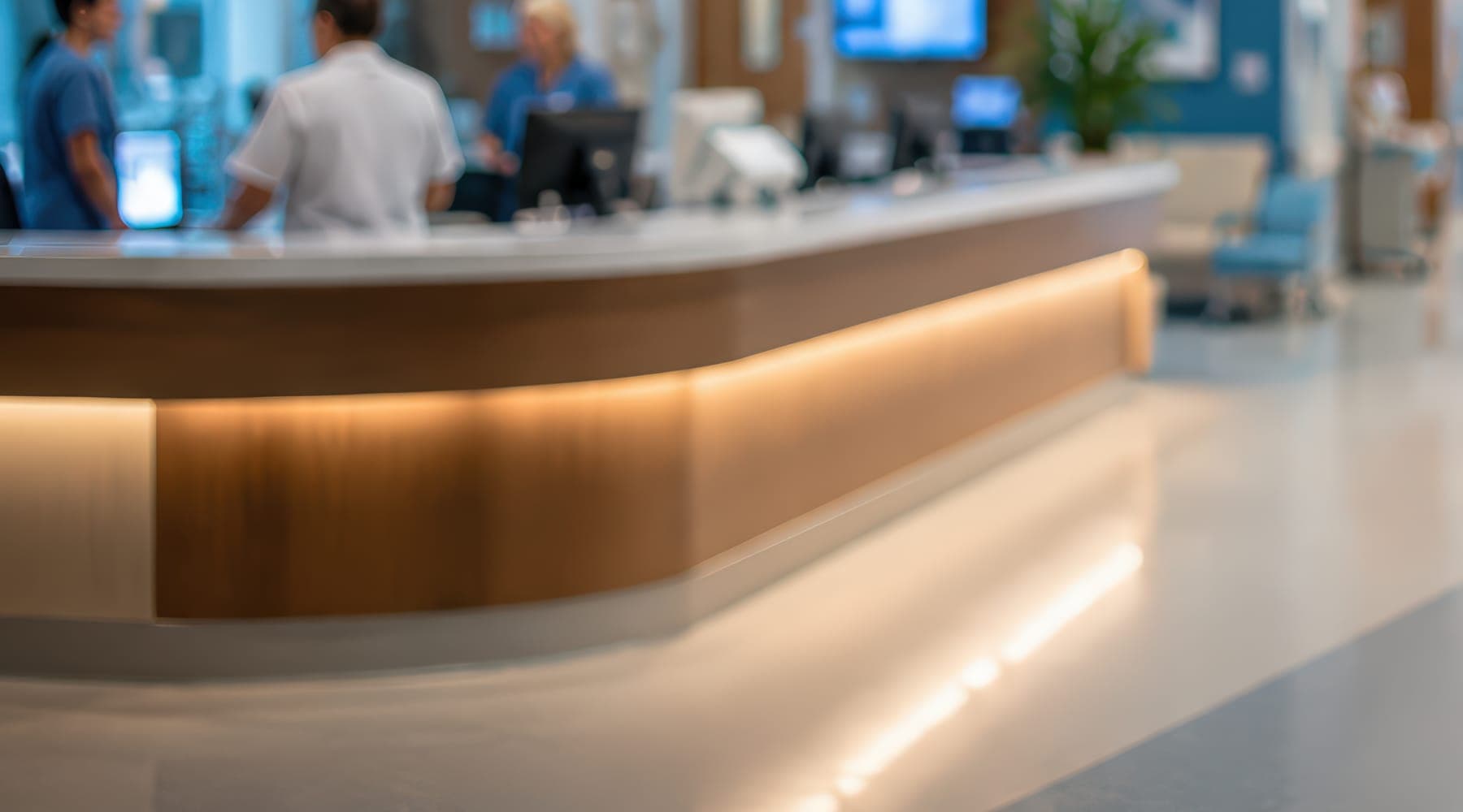 A hospital reception desk in use, staff working behind it out of focus