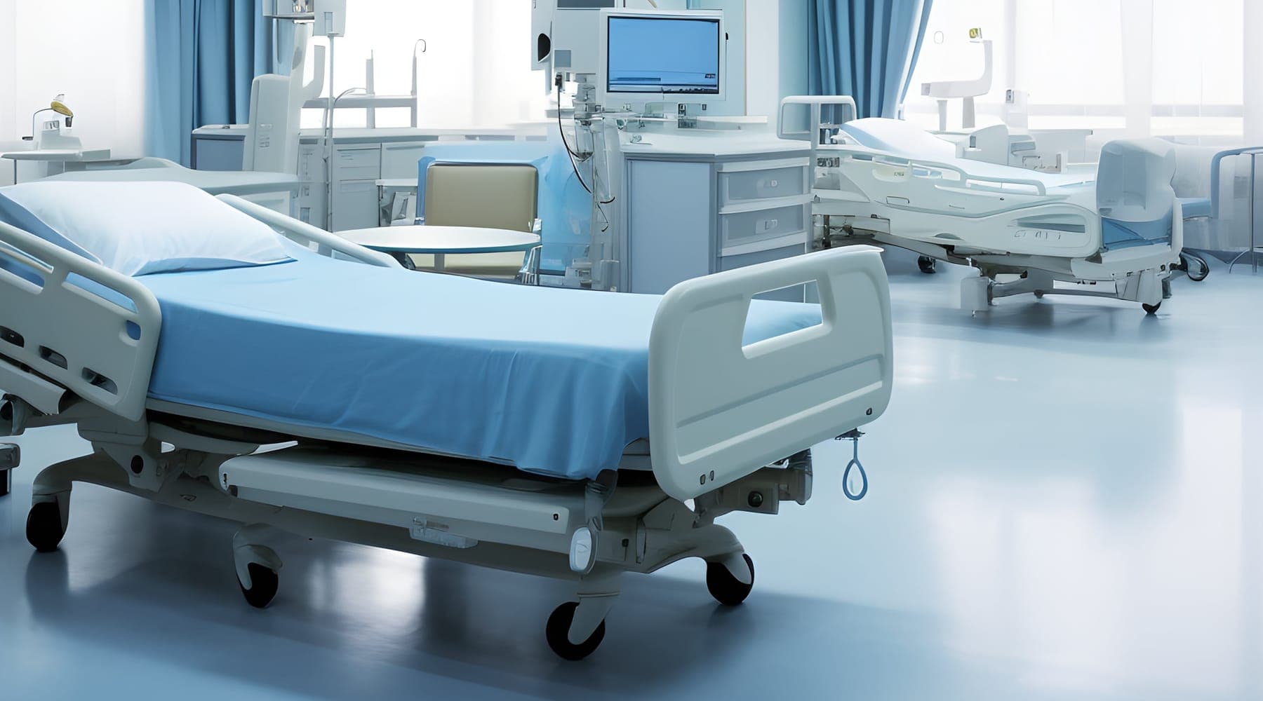 An empty inpatient ward with made beds, bedside monitors and blue privacy curtains